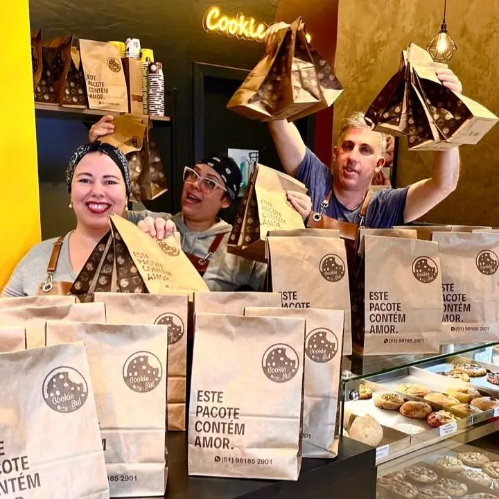 Os sócios da Cookie Sul no balcão, segurando os pacotes de delivery “Este pacote contém amor”